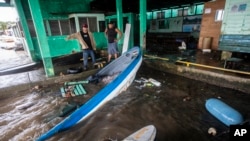 Des pêcheurs regardent des bateaux partiellement immergés dans l'eau après que l'ouragan Julia a frappé la région de Bluefields, au Nicaragua, le dimanche 9 octobre 2022. (AP Photo/Inti Ocon)