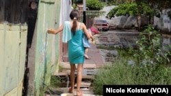 Une femme avec un bébé dans les bras marche prudemment à travers des planches pour atteindre sa maison sans marcher sur l'eau.
