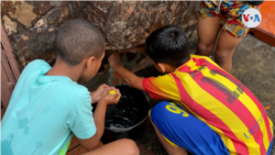 Deux garçons vénézuéliens préparent leurs pompes à eau en tas dans leur quartier pendant que leurs camarades de jeu attendent de les rejoindre. [Foto: Nicole Kolster/VOA]