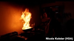 Un cuisinier chinois au Venezuela jette un morceau de poulet dans une poêle à frire qu'il secoue vigoureusement et met le feu.
