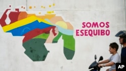 Un garçon conduit une moto devant une fresque représentant la carte vénézuélienne avec le territoire d'Essequibo inclus dans le quartier 23 de Enero de Caracas, Venezuela, le lundi 11 décembre 2023.