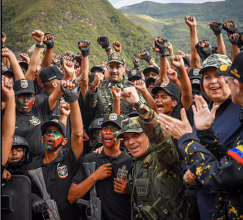 Un groupe d'hommes et de femmes, certains portant des vêtements de camouflage et du maquillage, lèvent le poing autour de Nicolas Maduro, avec un paysage montagneux en arrière-plan.