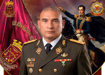 Portrait d'un homme chauve en uniforme et décorations militaires vert foncé, devant un drapeau rouge et l'image de Simón Bolívar à cheval