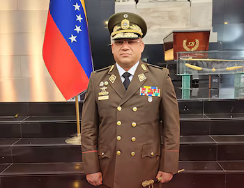 Le général Carlos Alexander Gómez Lárez, vêtu d'un uniforme militaire marron et de décorations, pose devant le drapeau vénézuélien
