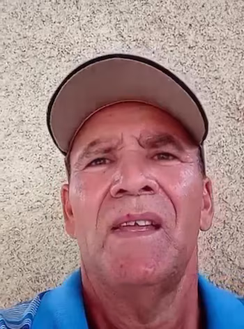 Gros plan d'un homme mûr à la peau claire portant une casquette beige et un polo bleu, regardant directement la caméra sur un fond texturé