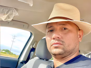 Gros plan d'Oswaldo José Cheremo Carrasquel, un homme avec un chapeau de paille et une barbe, assis sur le siège passager d'une voiture