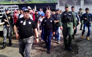 Un groupe d'hommes, dont Freddy Bernal et Miguel Domínguez, certains en uniforme militaire et d'autres en civil, marchent dans une rue craquelée