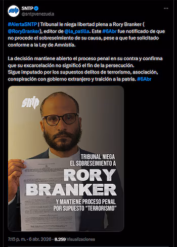 Un homme avec une barbe et des lunettes, Rory Branker, tient un document juridique avec un logo et lit derrière lui un grand texte sur le refus de son licenciement.