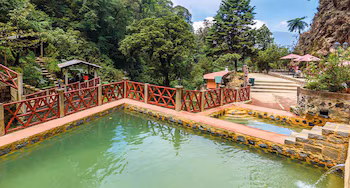 Piscines thermales d'eau verte avec balustrades rouges. Entouré de sentiers en pierre, d'arbres feuillus, de végétation et de petites structures avec parasols