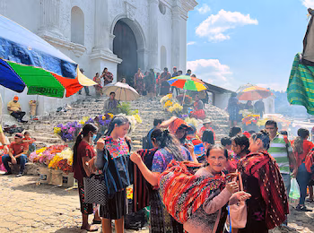 Marché animé à Chichicastenango. De nombreuses personnes en tenue traditionnelle, des stands avec des fleurs colorées et des parapluies, devant la façade d'une église blanche