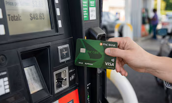 Gros plan d'une main insérant une carte de crédit Visa de la PNC Bank dans une pompe à essence affichant un total de 48,63 $ à l'écran