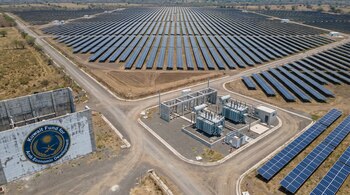 Photographie aérienne d'une vaste centrale solaire photovoltaïque au Salvador avec des rangées de panneaux bleus, des routes, une sous-station et le logo du Fonds Koweït sur un mur.