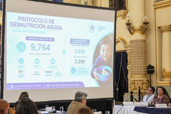 Écran de projection avec infographie sur la malnutrition aiguë au Guatemala, montrant du texte, des chiffres, des graphiques et l'image d'un enfant. Plusieurs personnes assises assistent à la présentation