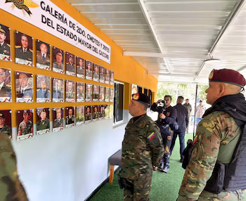 Deux soldats en uniforme de camouflage et bérets marron et noirs regardent un mur avec plusieurs portraits militaires encadrés