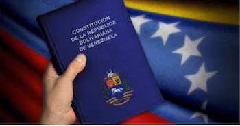 Gros plan d'une main tenant la Constitution de la République bolivarienne du Venezuela, avec les armoiries nationales, sur un drapeau vénézuélien