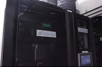Trois racks de serveurs noirs avec maillage, logos Isertec, Schneider Electric et Acer, un écran avec données et conduits de ventilation
