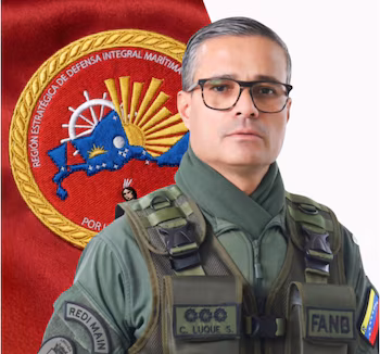 Portrait d'homme avec des lunettes, uniforme militaire vert, gilet tactique, patchs "REDI PRINCIPAL", "FANB", "C. LUQUE S." et drapeau du Venezuela. Fond rouge avec emblème naval
