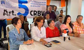 Groupe de personnes lors d’une réunion assises et debout. Un panneau blanc dit "Comité National de Promotion de la Défense de la Constitution, Art. 5 CRBV". un micro