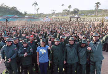 Foule de gens en uniformes verts et chapeaux de seau. Beaucoup ont levé les poings. Femme avec t-shirt bleu et carte du Venezuela. Palmiers et tentes
