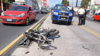 Moto tombée au sol dans la rue. Un véhicule de police bleu et une voiture rouge garée. Trois hommes debout sur la route