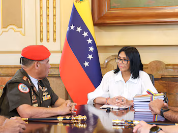 Delcy Rodríguez et un soldat avec un béret rouge parlent assis à une table avec le drapeau vénézuélien en arrière-plan