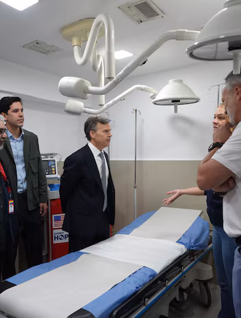 Plusieurs personnes discutent à côté d'une civière dans une zone médicale équipée de scialytiques articulés et d'équipements d'assistance