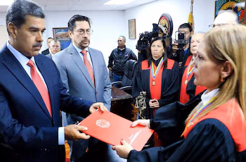 Nicolás Maduro, vêtu d'un costume sombre, remet un dossier rouge à Cilia Flores, qui porte une toge judiciaire. D'autres officiels et caméras sont présents