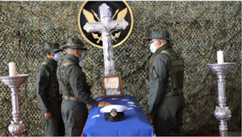 Trois soldats en uniforme vert et masqués gardent un cercueil recouvert d'un drapeau bleu avec des étoiles et une casquette navale blanche