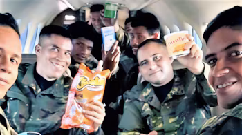 Des hommes en uniforme de camouflage posent à l’intérieur d’un avion tout en tenant un sac de chips et des contenants de nourriture