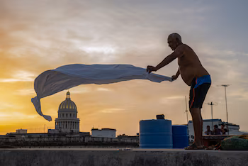 Alexis Mijan arrange les draps d'un lit de fortune sur le toit d'un immeuble résidentiel au crépuscule dans la Vieille Havane, le 12 août 2026. De nombreux Cubains dorment dehors pendant les nuits d'été, cherchant à se soulager des températures élevées et des fréquentes coupures de courant. (Photo de YAMIL LAGE / AFP)