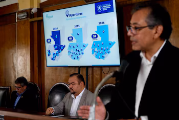 Un homme s'exprime sur un podium devant un écran montrant des cartes du Guatemala avec les chiffres des ouvertures de pharmacies de 2024 à 2026.