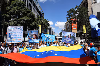 Des foules de personnes portent le drapeau du Venezuela et des banderoles à l'effigie de María Corina Machado lors d'une manifestation dans une rue urbaine