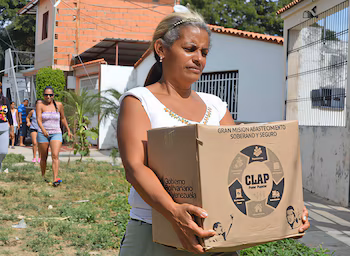 Une femme tient une boîte en carton avec le logo du programme CLAP et la légende Gouvernement bolivarien du Venezuela