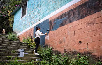 L'artiste salvadorienne Elizabeth Guardado efface une fresque représentant le gang MS (Mara Salvatrucha) avant la création d'une nouvelle œuvre d'art dans le cadre d'un festival d'art urbain dans la communauté 10 de Octubre de San Marcos, au Salvador, le 2 octobre 2026. Le projet artistique cherche à transformer l'identité d'une communauté historiquement affectée par la violence des gangs. (Photo de Marvin RECINOS / AFP)