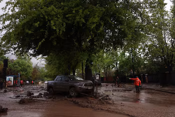 Une personne guide un cycliste dans une rue couverte de boue, à côté d'un véhicule concerné, après que de fortes pluies ont provoqué un glissement de terrain à Santiago, au Chili, le 8 octobre 2026 (REUTERS/Pablo Sanhueza)