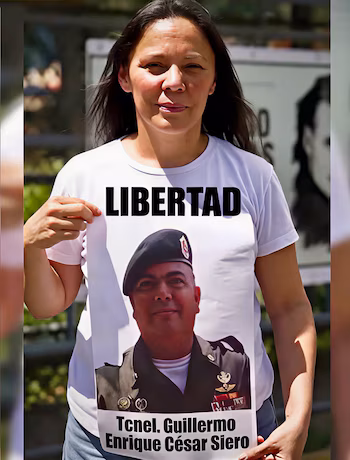 Une femme tient un t-shirt blanc avec le mot Freedom, l'image d'un soldat et le texte Tcnel. Guillermo Enrique César Siero