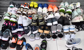Une grande pile de baskets de différentes couleurs et marques sont empilées au hasard. Des modèles de Nike, Adidas et Vans sont visibles